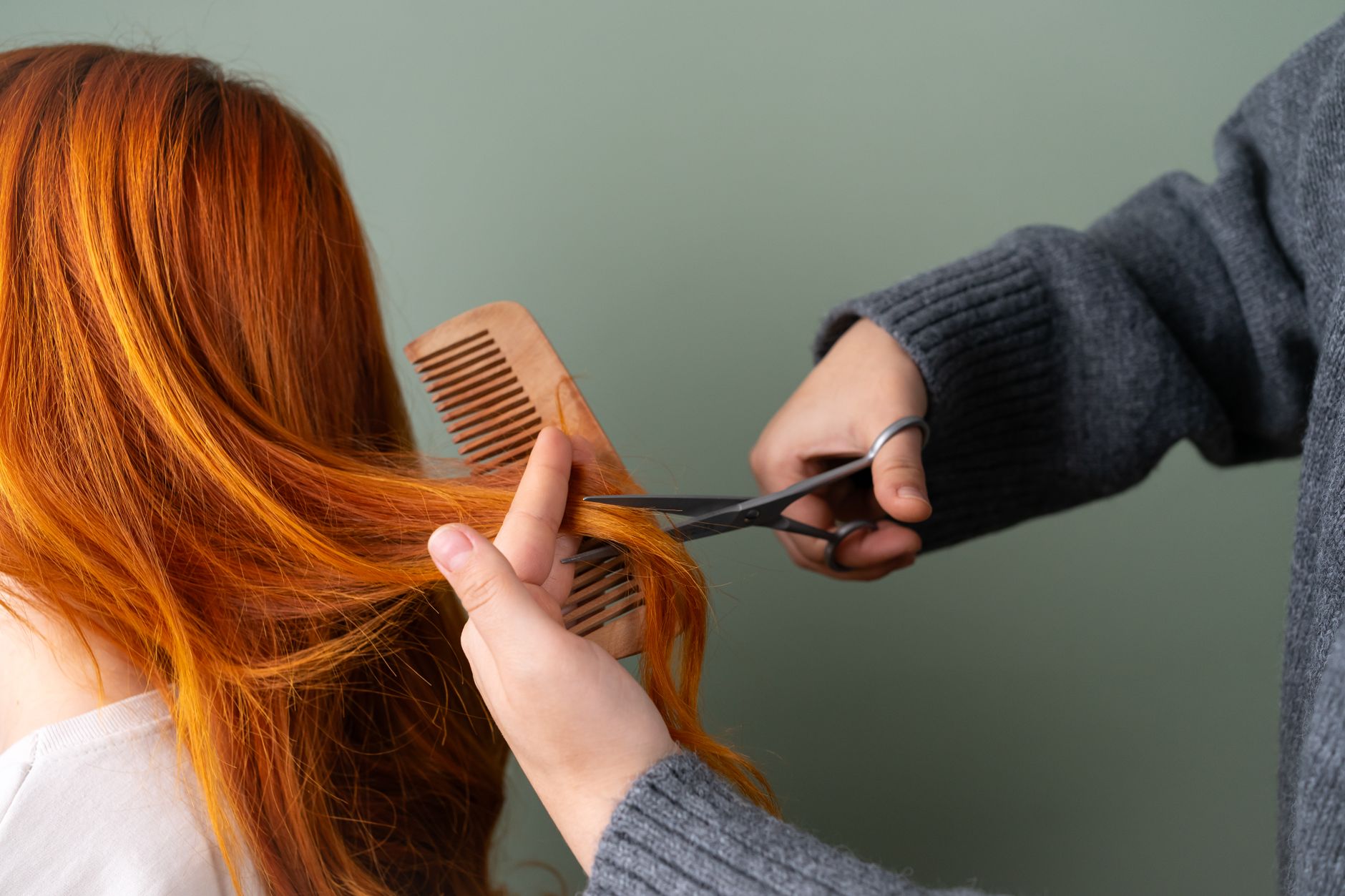 Stylist trimming a client's hair with scissors and a wooden comb